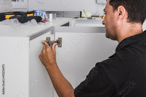 Worker adjusting the hinges of a kitchen cabinet photo