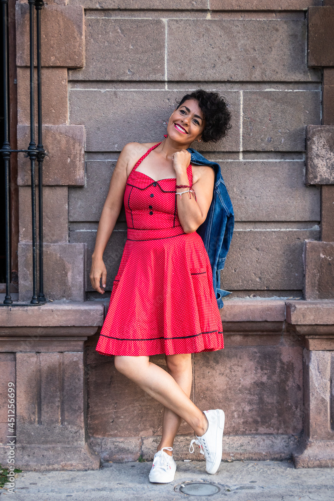 Mid adult afro mexican smiling woman wearing a red dress and white sneakers, leaning against a quarry wall Mid adult afro mexican smiling woman wearing a red dress and white sneakers, leaning against a quarry wall