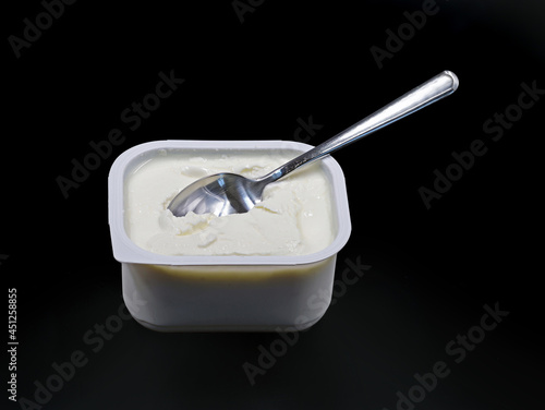 low-fat quark in plastic container with spoon isolated on black background photo