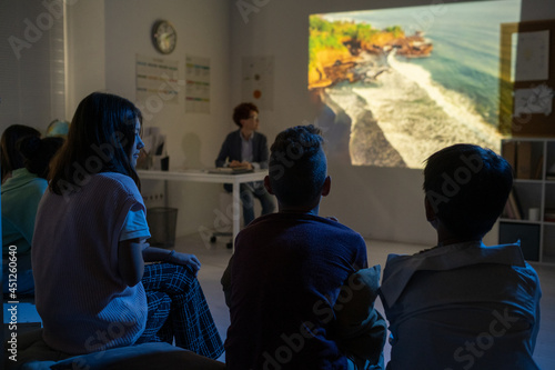 Foto Group of schoolkids watching video about natural environment in dark classroom