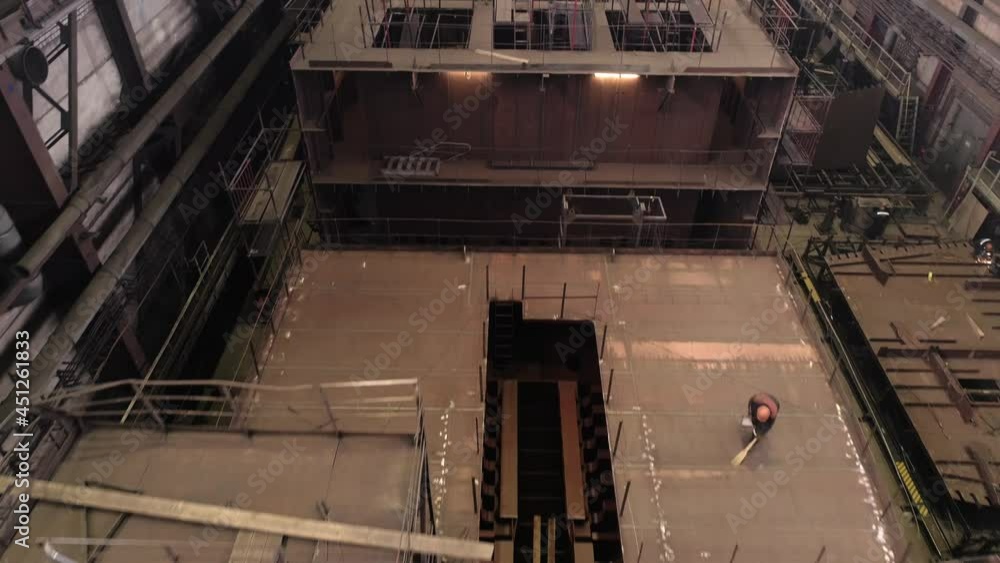 Scaffolds and holes on upper deck and worker sweeping restored crab ship in dry dock of industrial complex upper view Scaffolds and holes on upper deck and worker sweeping restored crab ship in dry dock of industrial complex upper view