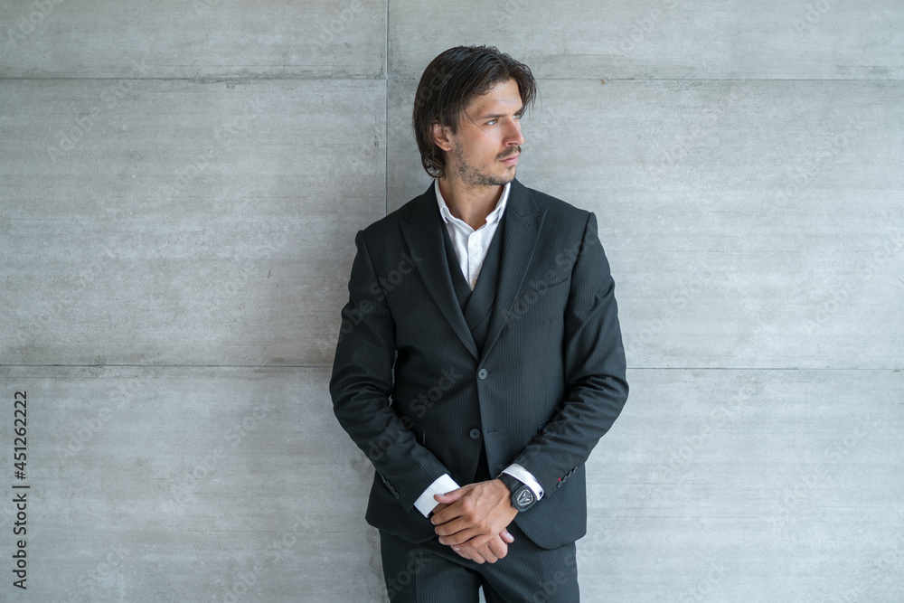 Stylish young brunet man in black suit standing on light grey background. Portrait. High quality photo Stylish young brunet man in black suit standing on light grey background. Portrait. High quality photo