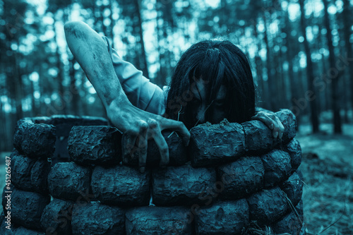 Girl in image of scary zombie crawls out of the stone well in dark forest. photo