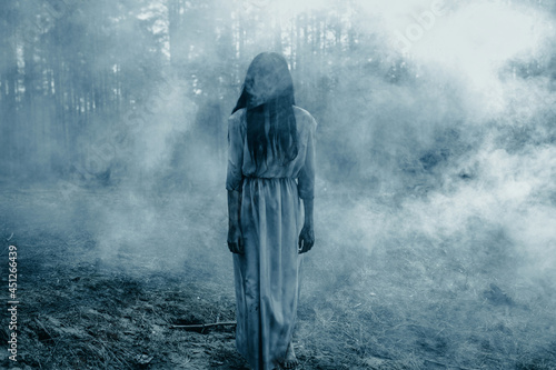 Foto Girl in image of scary zombie walks in dark forest among smoke.