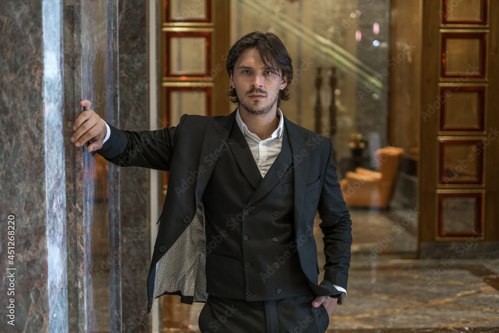 Portrait of handsome young business man wearing black classic suit standing near modern building. Looking at camera with copy space. Hand in pocket Portrait of handsome young business man wearing black classic suit standing near modern building. Looking at camera with copy space. Hand in pocket