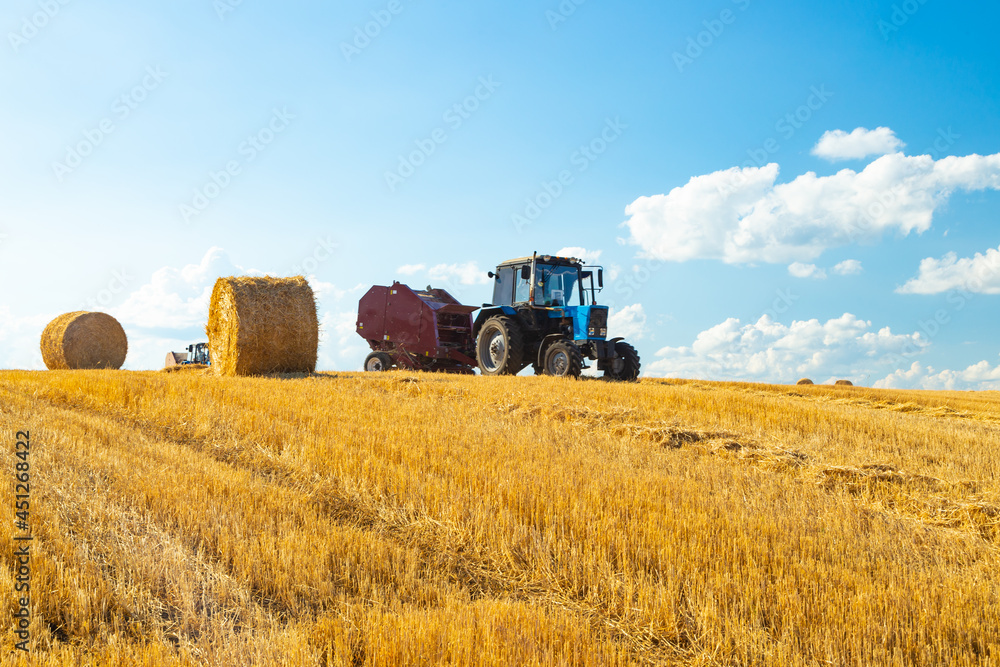 Fototapeta premium Bales of Hay in the Countryside and Tractor at Work in the background