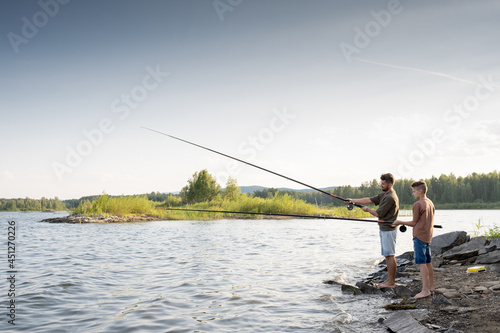 Two young barefoot men with rods standing in front of lake while fishing