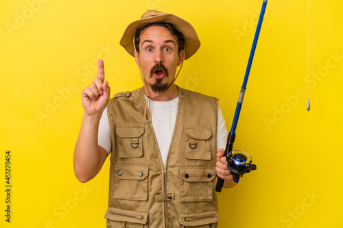 Young caucasian fisherman holding rod isolated on yellow background having some great idea, concept of creativity.
