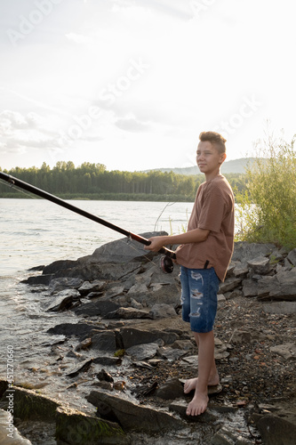 Active teenage boy with long rod standing by waterside while fishing on his own