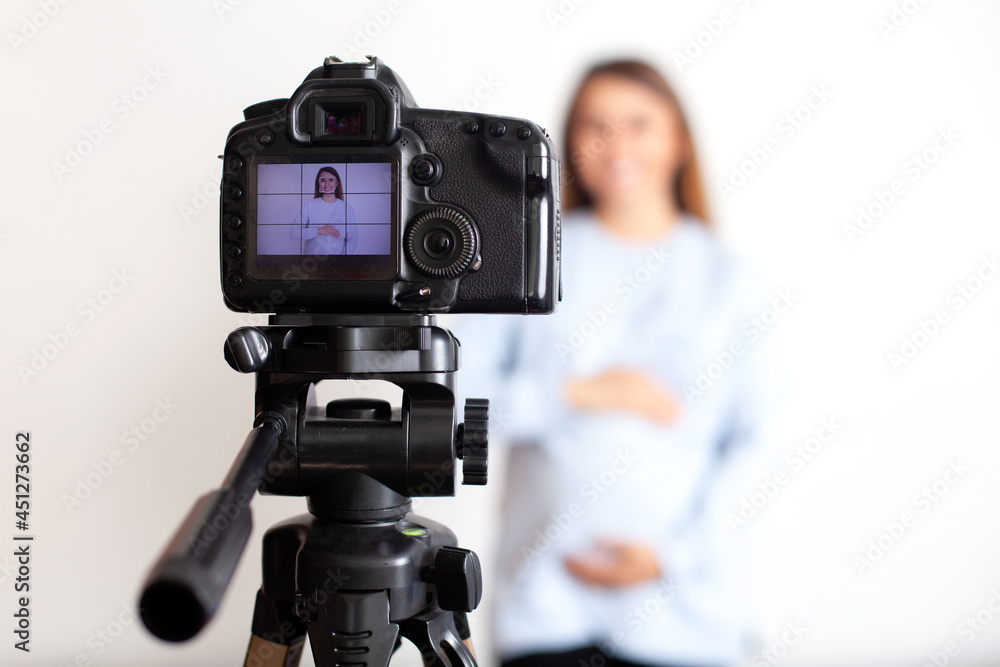 A beautiful pregnant blogger shoots video on camera on a tripod for her social networks. Blog about medicine and pregnancy. Like. Stream. White background.