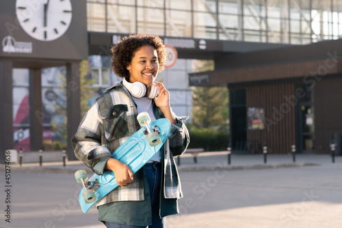 Smiling female teenager holding blue skateboard while standing against modern architecture © pressmaster