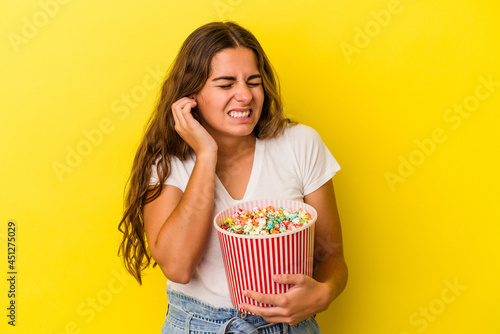 Young caucasian woman holding a popcorns isolated on yellow background covering ears with hands.