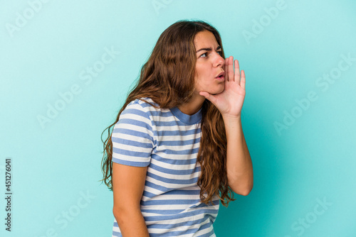 Young caucasian woman isolated on blue background is saying a secret hot braking news and looking aside