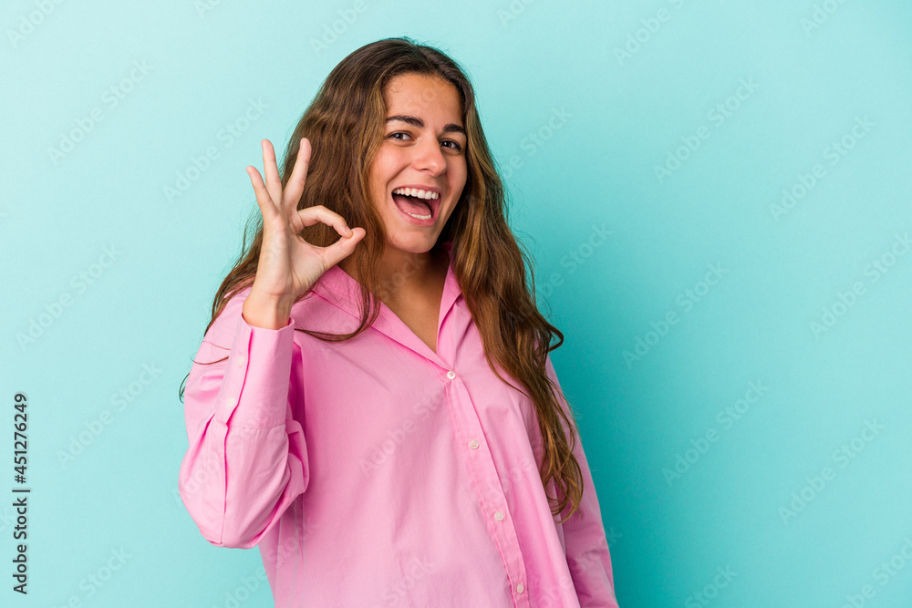 Young caucasian woman isolated on blue background cheerful and confident showing ok gesture. Young caucasian woman isolated on blue background cheerful and confident showing ok gesture.
