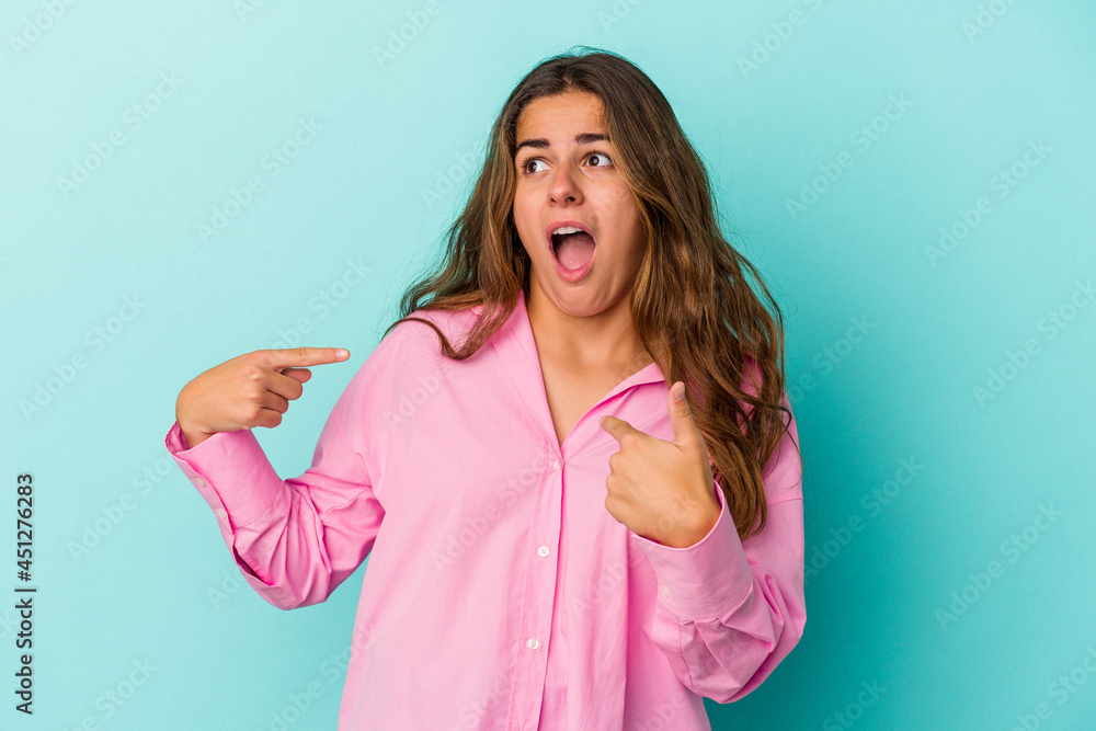 Young caucasian woman isolated on blue background surprised pointing with finger, smiling broadly. Young caucasian woman isolated on blue background surprised pointing with finger, smiling broadly.