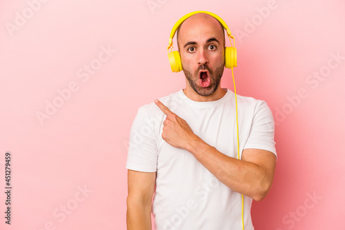 Young caucasian bald man listening to music isolated on pink background pointing to the side