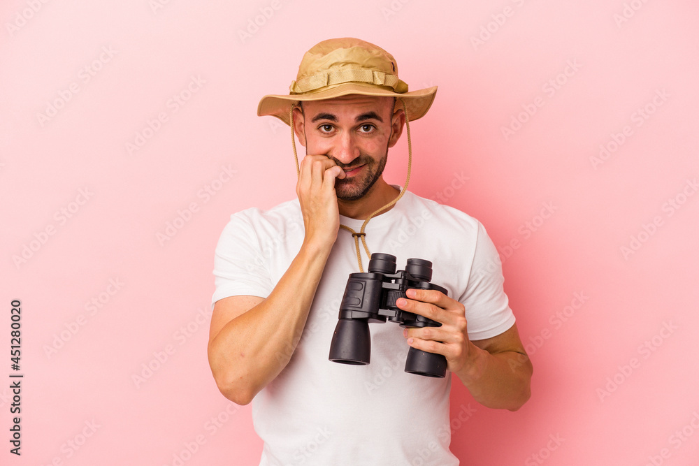 Young caucasian bald man holding binoculars isolated on pink background biting fingernails, nervous and very anxious. Young caucasian bald man holding binoculars isolated on pink background biting fingernails, nervous and very anxious.