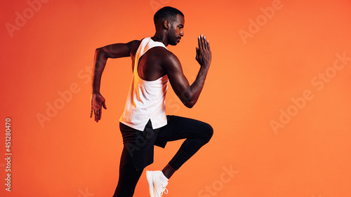 Side view of a male runner sprinting over orange background