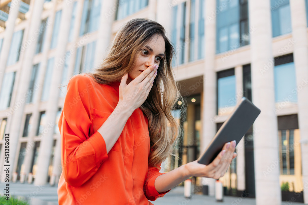 Caucasian woman holding a tablet in her hands and looking shocked Caucasian woman holding a tablet in her hands and looking shocked
