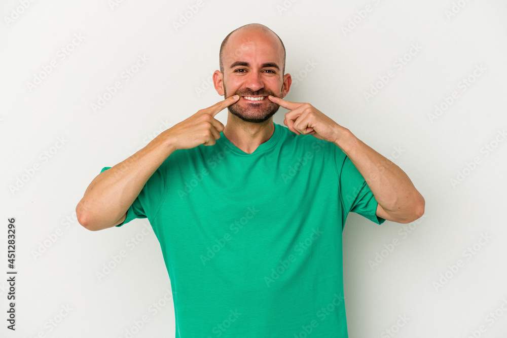 Young bald man isolated on white background smiles, pointing fingers at mouth. Young bald man isolated on white background smiles, pointing fingers at mouth.