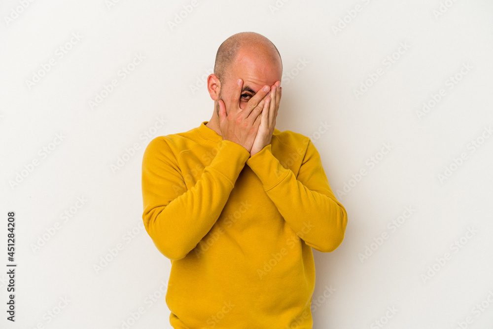 Young bald man isolated on white background blink at the camera through fingers, embarrassed covering face. Young bald man isolated on white background blink at the camera through fingers, embarrassed covering face.