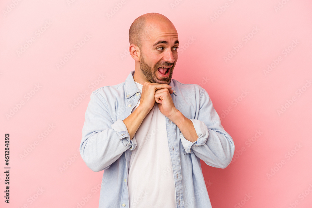 Young caucasian bald man isolated on pink background keeps hands under chin, is looking happily aside. Young caucasian bald man isolated on pink background keeps hands under chin, is looking happily aside.