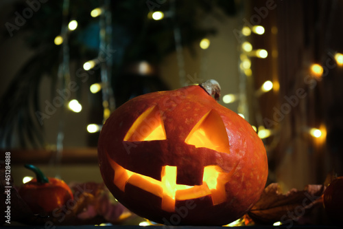 Halloween pumpkin head Jack o lantern. Carved pumpkin illuminated from inside, bokeh lights on background. Halloween home decoration. photo