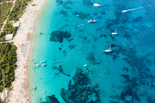 View from above, stunning aerial view of a green coastline with a white sand beach and and boats sailing on a turquoise water at sunset. Cala di volpe beach, Costa Smeralda, Sardinia, Italy...