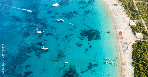 View from above, stunning aerial view of a green coastline with a white sand beach and and boats sailing on a turquoise water at sunset. Cala di volpe beach, Costa Smeralda, Sardinia, Italy...