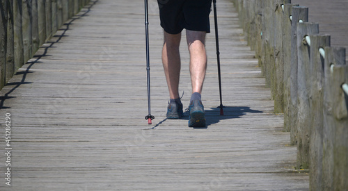 Homem a caminhar num passadiço com dois sticks de apoio - caminhada de longa distância photo