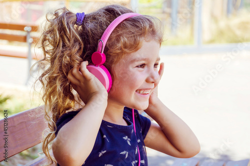 Happy Toddler Girl Listening Music Outdoor with Pink Headphones .Smiling Child Having Fun Outdoor. Selective Focus 