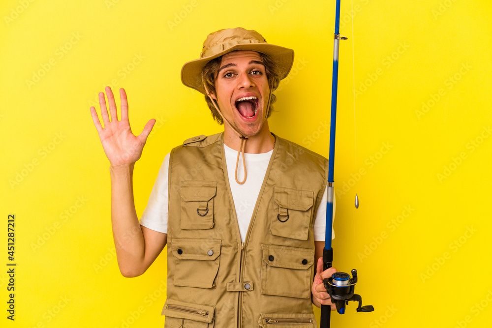 Young fisherman with makeup holding rod isolated on yellow background receiving a pleasant surprise, excited and raising hands. Young fisherman with makeup holding rod isolated on yellow background receiving a pleasant surprise, excited and raising hands.
