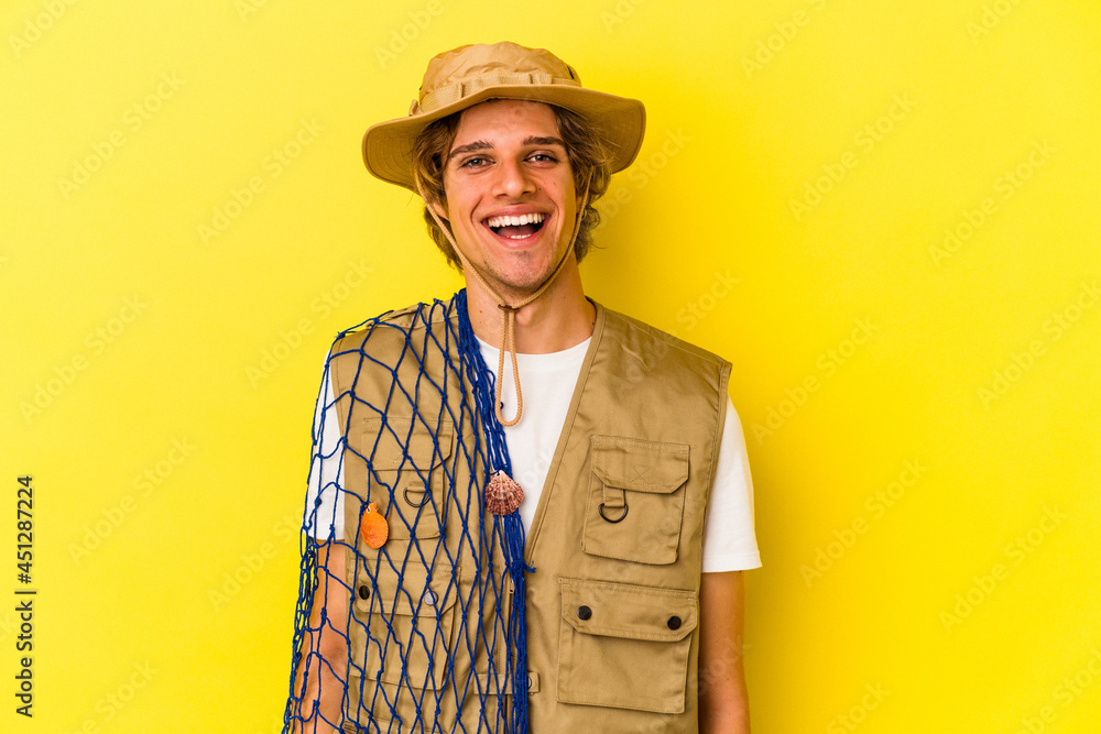 Young fisherman with makeup holding a net isolated on yellow background happy, smiling and cheerful. Young fisherman with makeup holding a net isolated on yellow background happy, smiling and cheerful.
