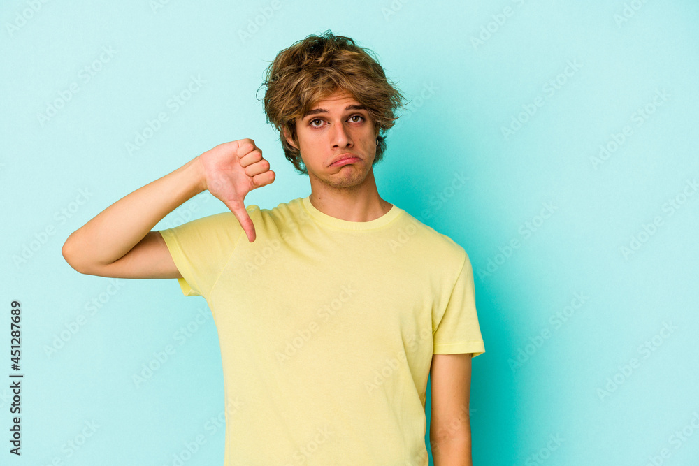 Young caucasian man with make up isolated on blue background showing a dislike gesture, thumbs down. Disagreement concept. Young caucasian man with make up isolated on blue background showing a dislike gesture, thumbs down. Disagreement concept.
