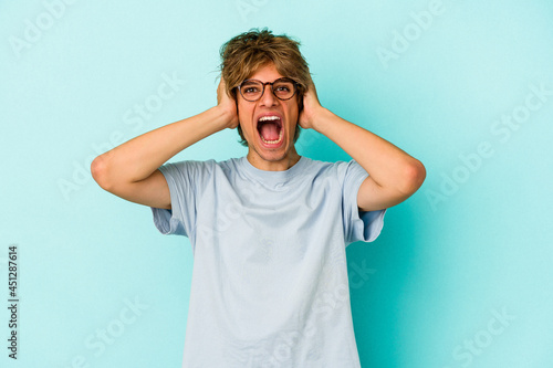 Young caucasian man with make up isolated on blue background screaming, very excited, passionate, satisfied with something.
