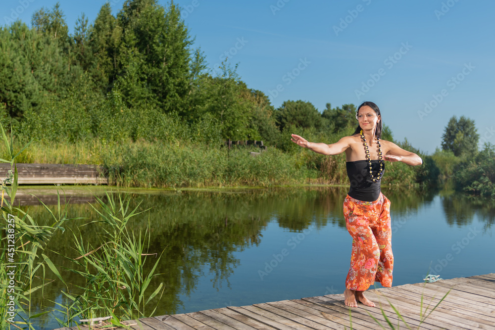 Fototapeta premium Girl with dark hair doing yoga on the lake in summer on a sunny day