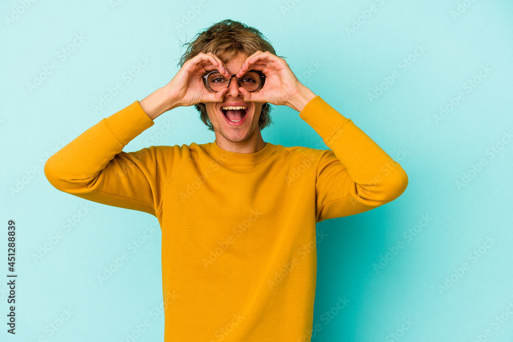 Young caucasian man with make up isolated on blue background showing okay sign over eyes Young caucasian man with make up isolated on blue background showing okay sign over eyes