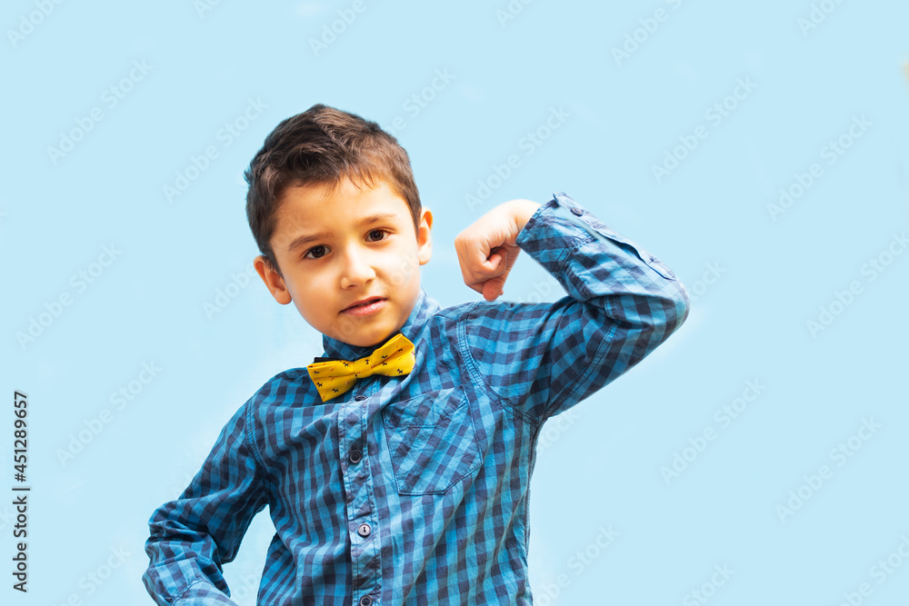 boy shows strength with a gesture. portrait of a beautiful boy on a blue background boy shows strength with a gesture. portrait of a beautiful boy on a blue background