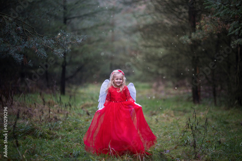 Weihnachtsengel in einem Märchen Wald. Es liegt kein Schnee. Typisch Europa, öfter mal kein Schnee am Weihnachten. Trotzdem es ist weihnachtlich. Hält ihr Kleid fest und lacht.