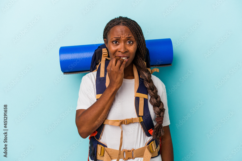 Young african american hiker woman isolated on blue background biting fingernails, nervous and very anxious. Young african american hiker woman isolated on blue background biting fingernails, nervous and very anxious.