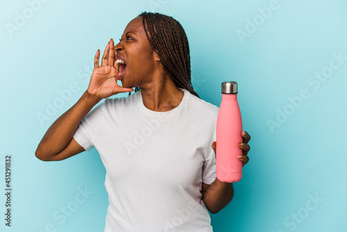 Young african american woman holding canteen isolated on blue background shouting and holding palm near opened mouth.