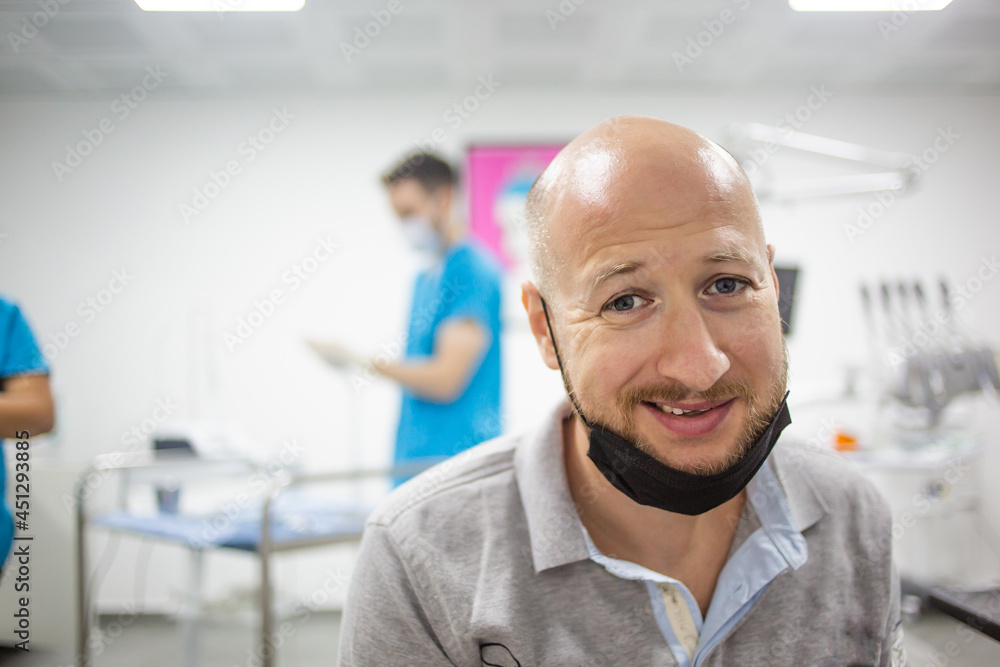 Fototapeta premium Scared caucasian male with mask in a dental clinic is waiting for a teeth check up. Nurse and dental care equipment on the background