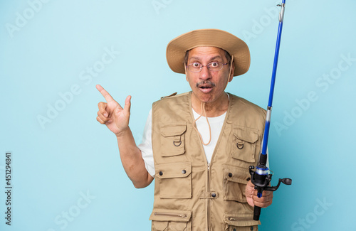 Senior indian fisherman holding rod isolated on blue background pointing to the side