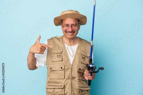 Senior indian fisherman holding rod isolated on blue background person pointing by hand to a shirt copy space, proud and confident