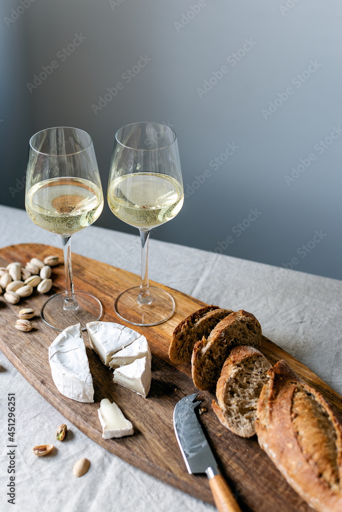 Two glasses of white wine and a wooden board with appetizers on the table. Two glasses of white wine and a wooden board with appetizers on the table.