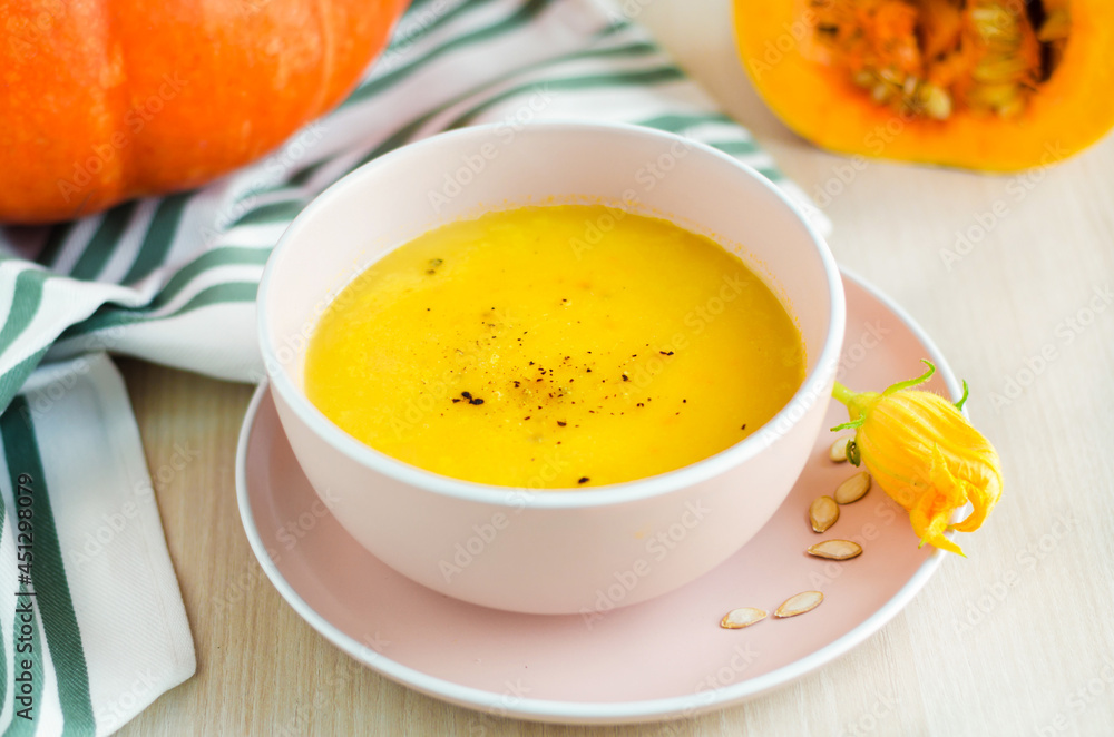 creamy pumpkin soup with vegetables, spice, seeds and croutons in a bowl on light wooden background. Thanksgiving Day. traditional autumn dish, menu on the table. soft focus creamy pumpkin soup with vegetables, spice, seeds and croutons in a bowl on light wooden background. Thanksgiving Day. traditional autumn dish, menu on the table. soft focus