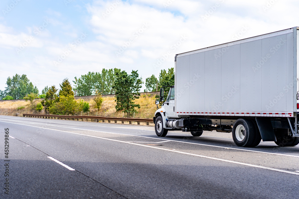 White day cab medium duty semi truck with big box trailer running on the highway road entrance line. White day cab medium duty semi truck with big box trailer running on the highway road entrance line.