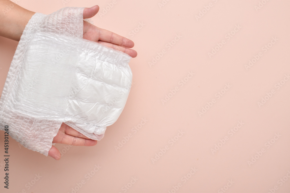 An adult hand pulls a diaper-panties on a beige background. Pesto for the text. a place to copy. Flat layout, top view An adult hand pulls a diaper-panties on a beige background. Pesto for the text. a place to copy. Flat layout, top view