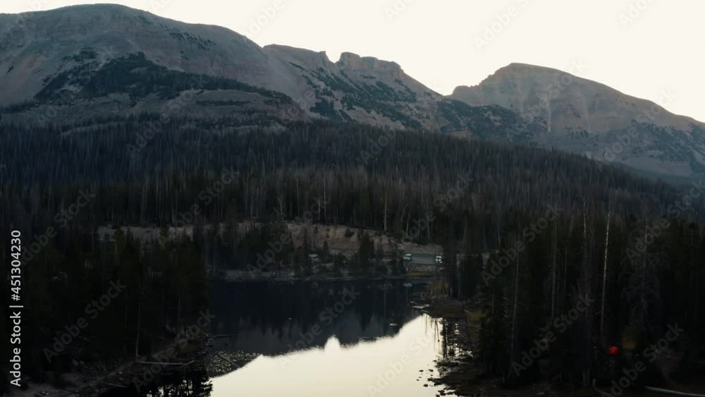 rising Aerial drone shot of the tranquil Butterfly Lake with lily pads up the Uinta National Forest in Utah with large Rocky Mountains and pine trees surrounding on a foggy summer morning. rising Aerial drone shot of the tranquil Butterfly Lake with lily pads up the Uinta National Forest in Utah with large Rocky Mountains and pine trees surrounding on a foggy summer morning.