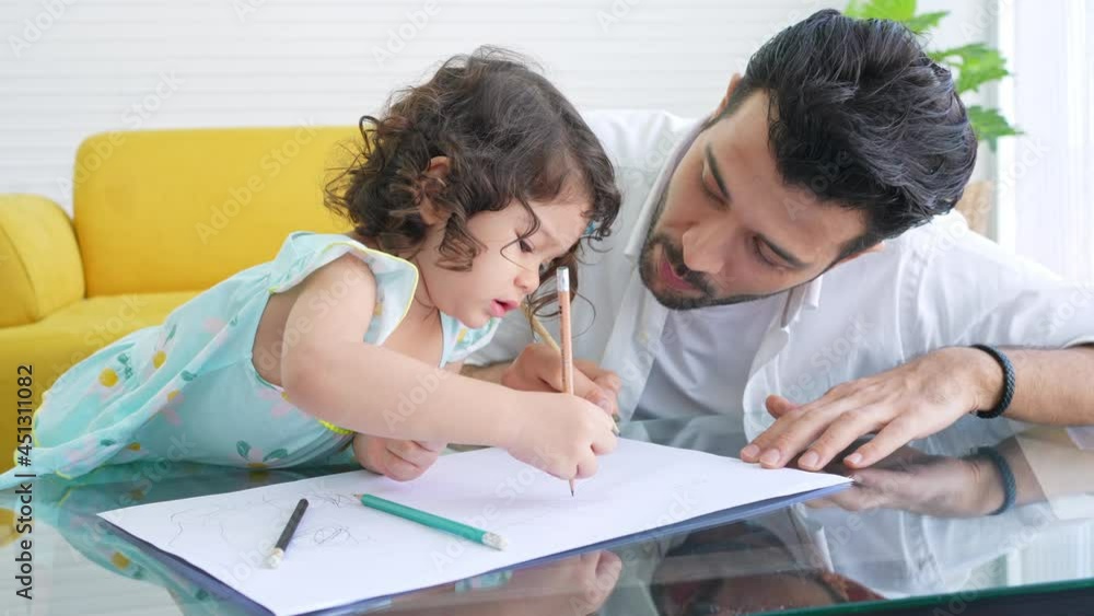 Happy family father teach little daughter using color pencil drawing on paper book in living room. Dad and cute child girl kid enjoy and having fun leisure activity and homeschooling together at home Happy family father teach little daughter using color pencil drawing on paper book in living room. Dad and cute child girl kid enjoy and having fun leisure activity and homeschooling together at home